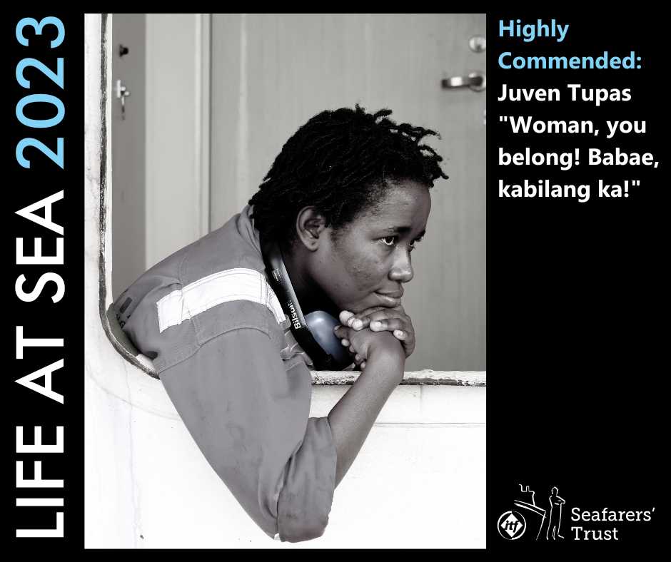 A graphic showing a Highly Commended Prize photo on a black background with text reading Life At Sea 2023 Highly Commended Juven Tupas "Woman You Belong! Babae, kabilang ka!". The photo is a monochrome portrait of a black woman seafarer, sat leaning with her elbow over a rail and looking out towards the right of the photo. She is wearing an overall and has ear defenders around her neck.