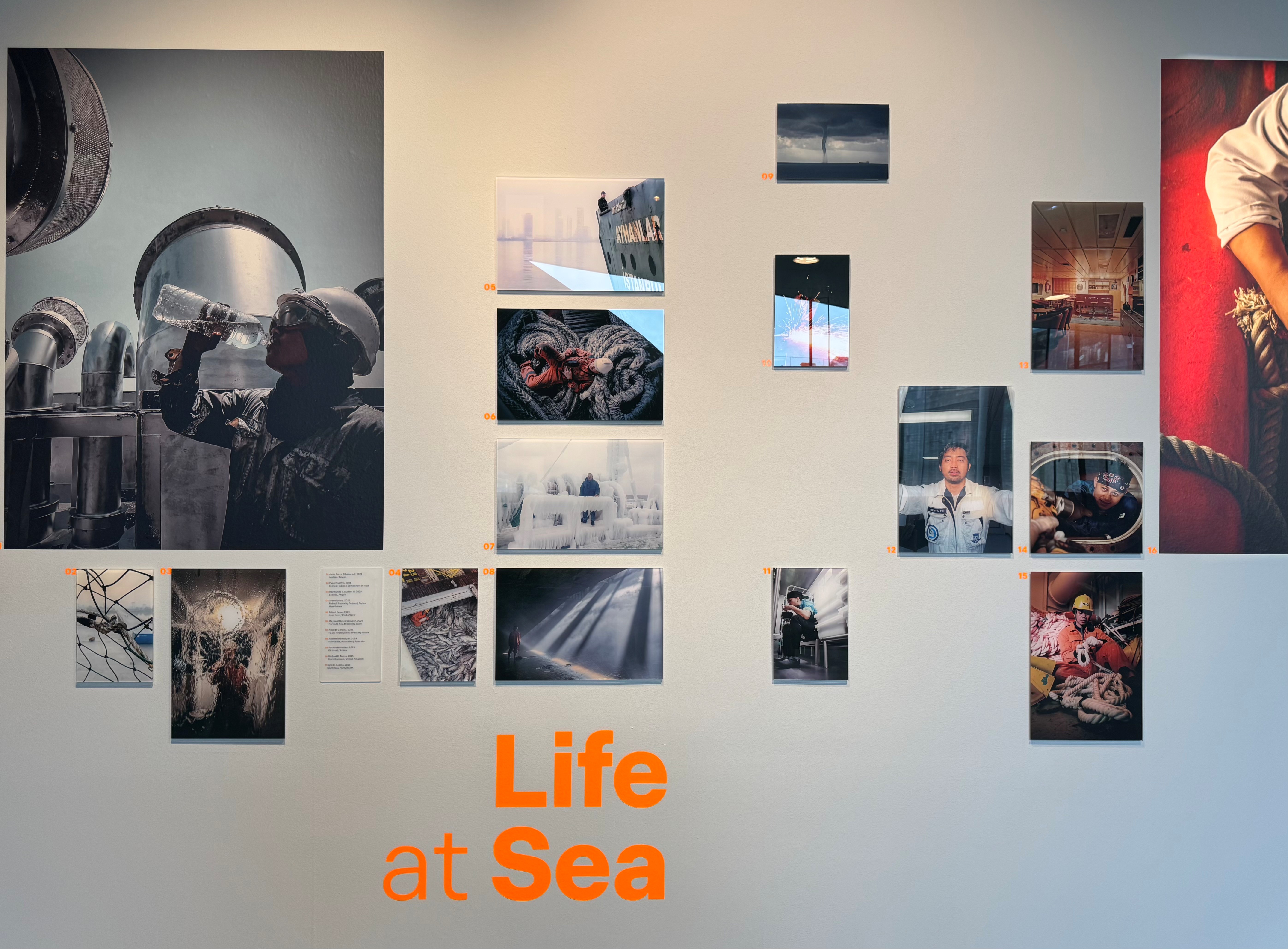 The wall of the exhibition with pictures of various sizes and the Life At Sea title text.