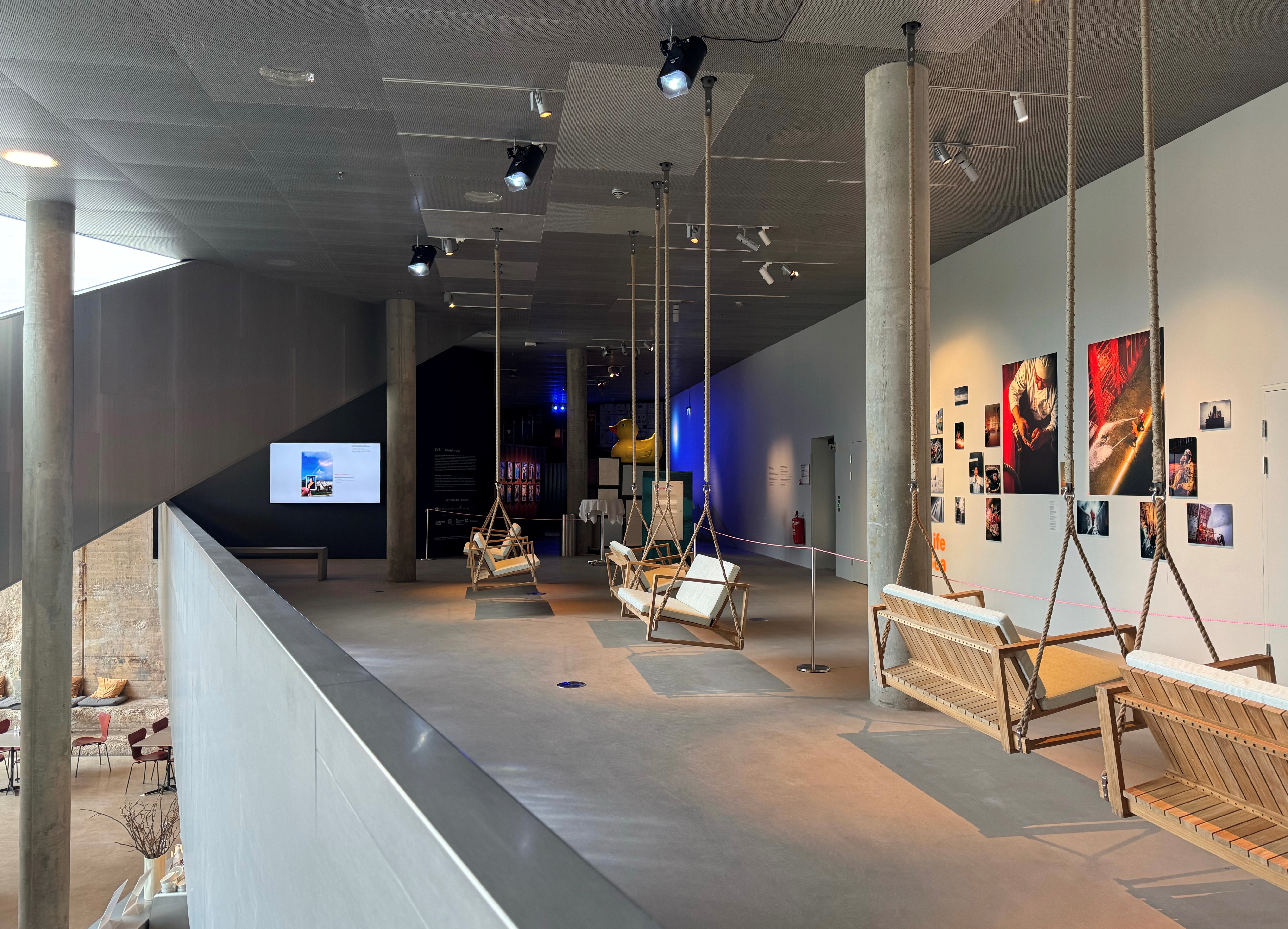 A view of the Deck exhibition space with the Life At Sea Exhibition showing the swing chairs suspended from the ceiling and the exhibition in the background.